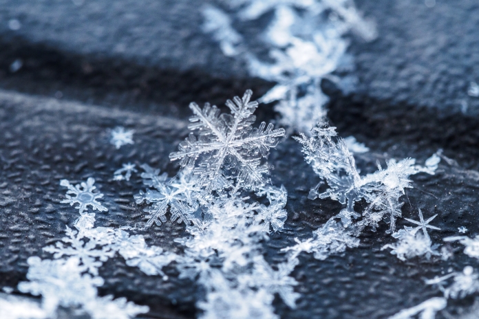 Um floco de neve de placa, achatado e detalhado, com formas hexagonais e padrões delicados que lembram uma joia intricada.