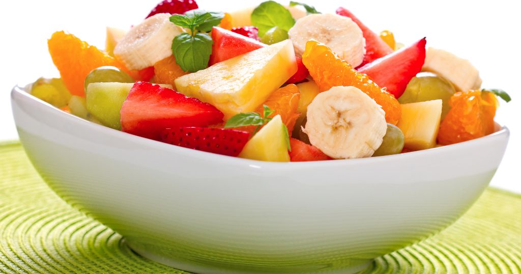 Foto de uma salada de frutas - Uma tigela colorida com pedaços de banana, maçã, laranja, morango e uva, apresentando uma refeição saudável e deliciosa.